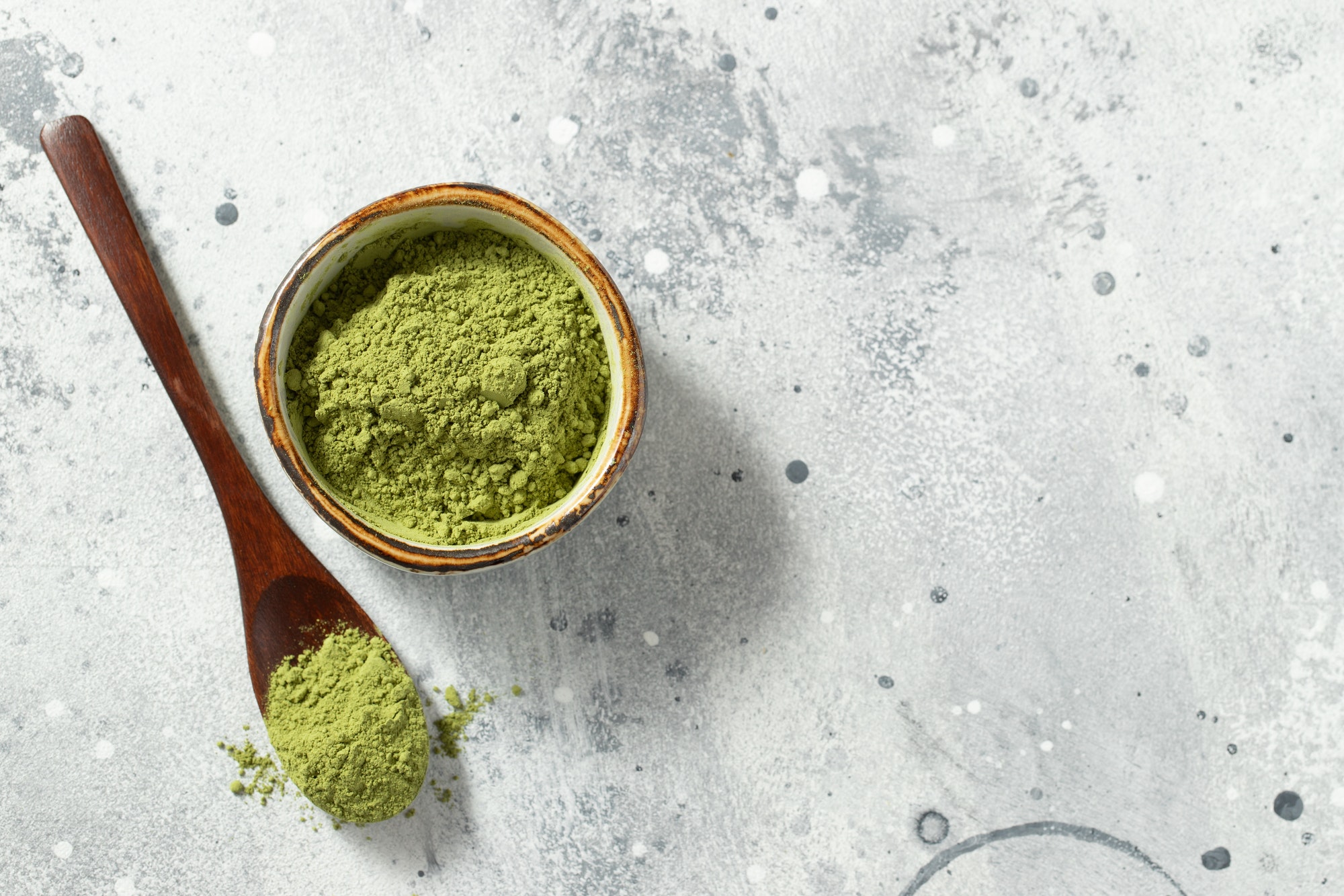 Green matcha tea powder with spoon on white concrete background.