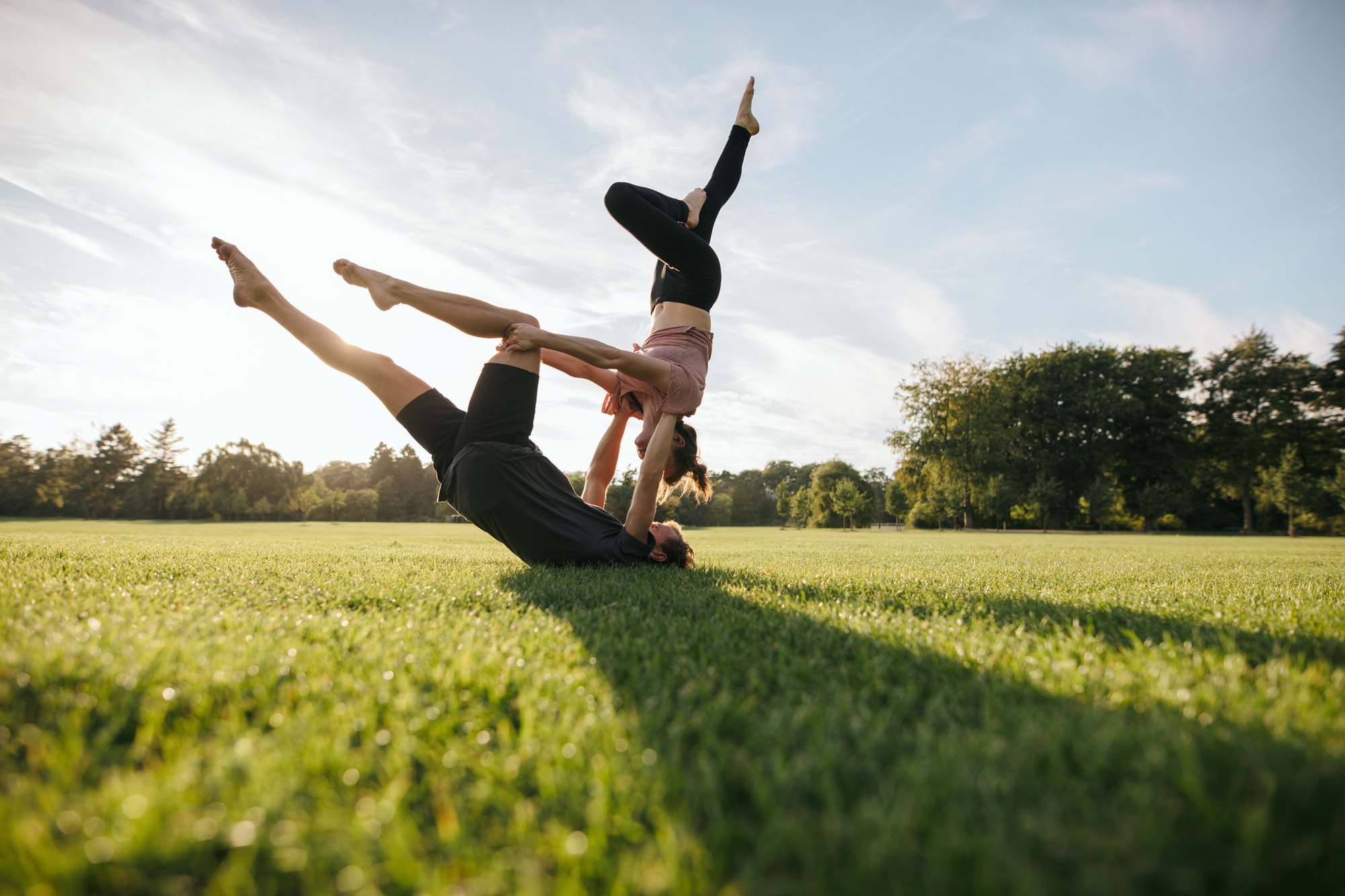 Healthy young couple doing acro yoga on grass
